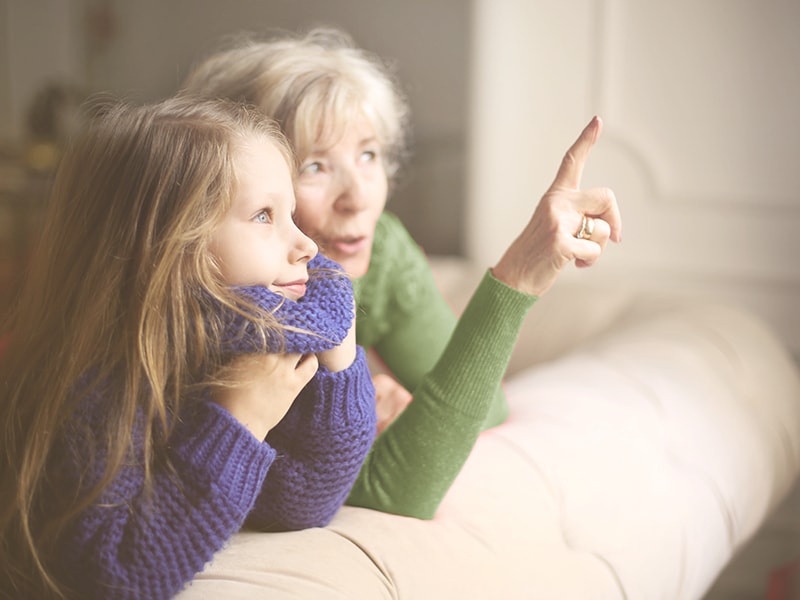 A woman pointing outside a window with a child at her side
